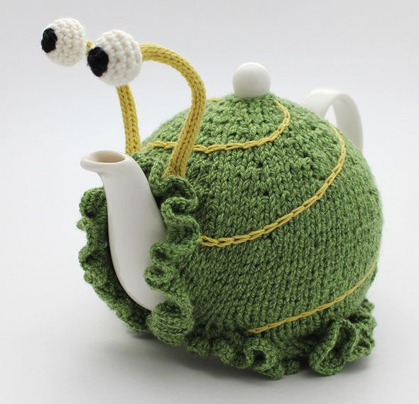 A white ceramic teapot wearing a green knitted tea cosy designed to look like a whimsical snail. The cosy features yellow lines mimicking a shell spiral, frilly edges around the base and spout, and two tall yellow stalks with crocheted eyes perched on top.
A white ceramic teapot wearing a green knitted tea cosy designed to look like a whimsical snail. The cosy features yellow lines mimicking a shell spiral, frilly edges around the base and spout, and two tall yellow stalks with crocheted eyes perched on top.